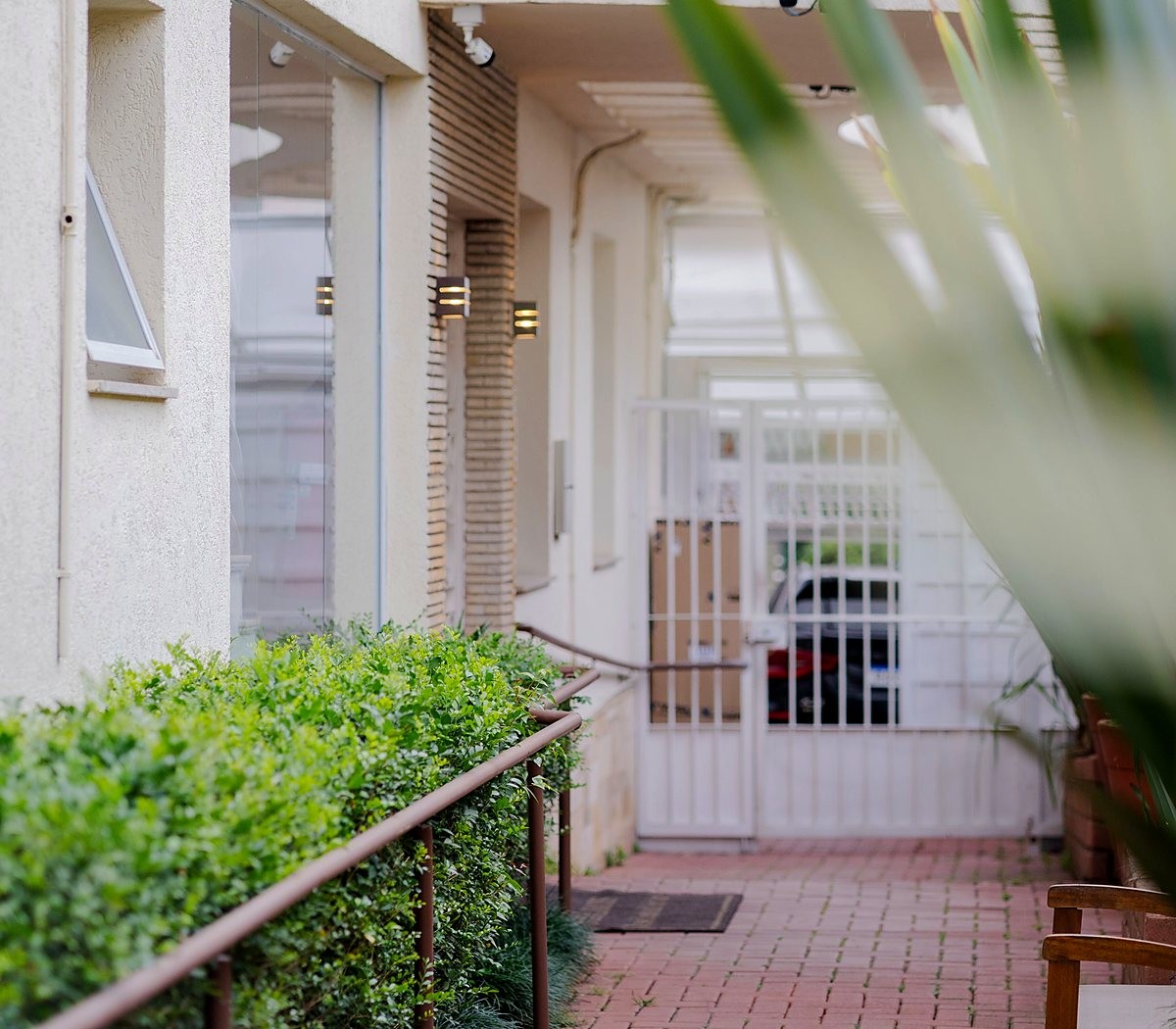 serv-pessoas Corredor de condomínio com jardim, grades e piso de tijolos